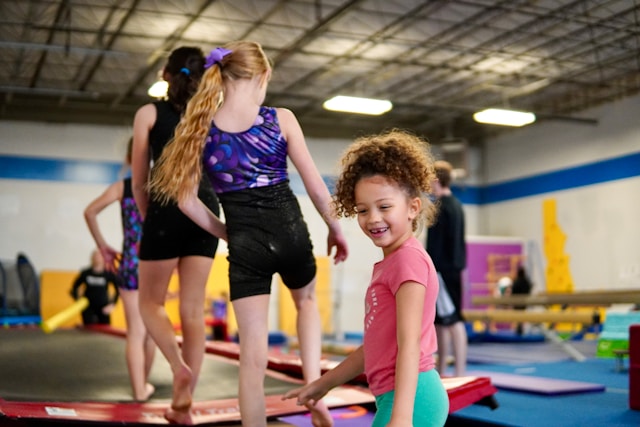Kinderturnen bij Turnclub Olympia Zwijnaarde - een jong meisje glimlacht terwijl zij en haar teamgenootjes op de fast track trainen. Een dynamische en stimulerende omgeving waar kinderen gymnastiekvaardigheden leren en plezier hebben. Ideaal voor de ontwikkeling van balans en coördinatie.
